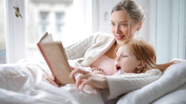 Mae le um livro para a filha na cama