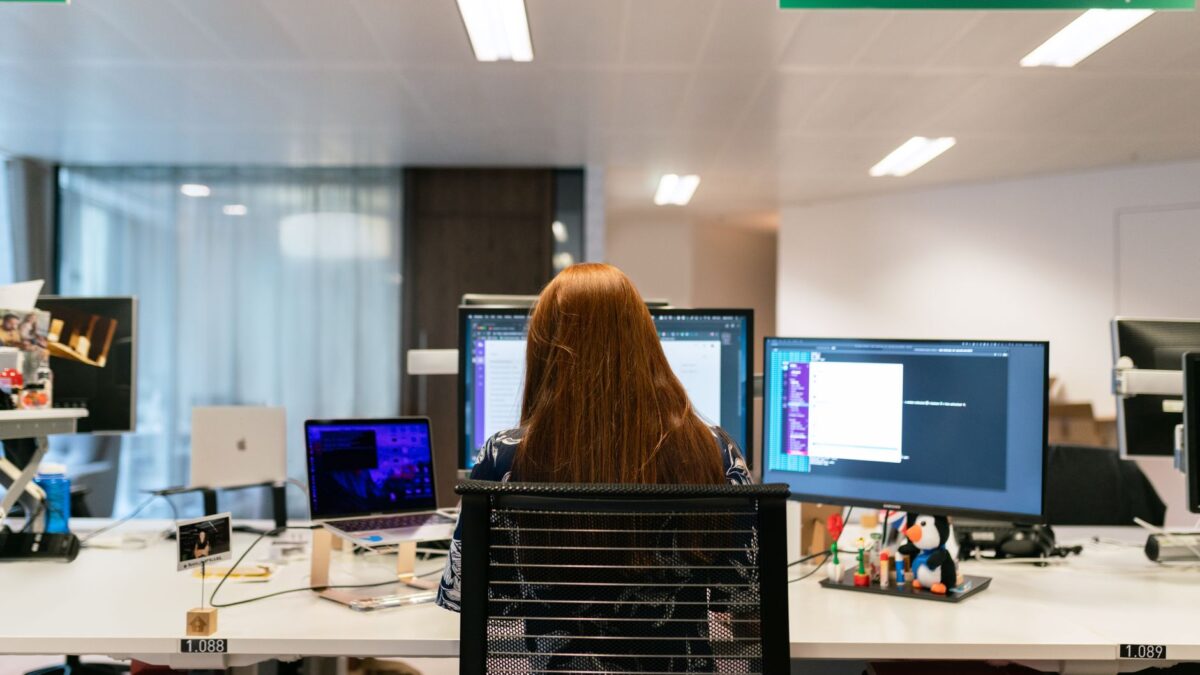 Profissional de tecnologia trabalhando em múltiplos monitores, ilustrando trabalhadores em visto H-1B