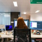 Profissional de tecnologia trabalhando em múltiplos monitores, ilustrando trabalhadores em visto H-1B