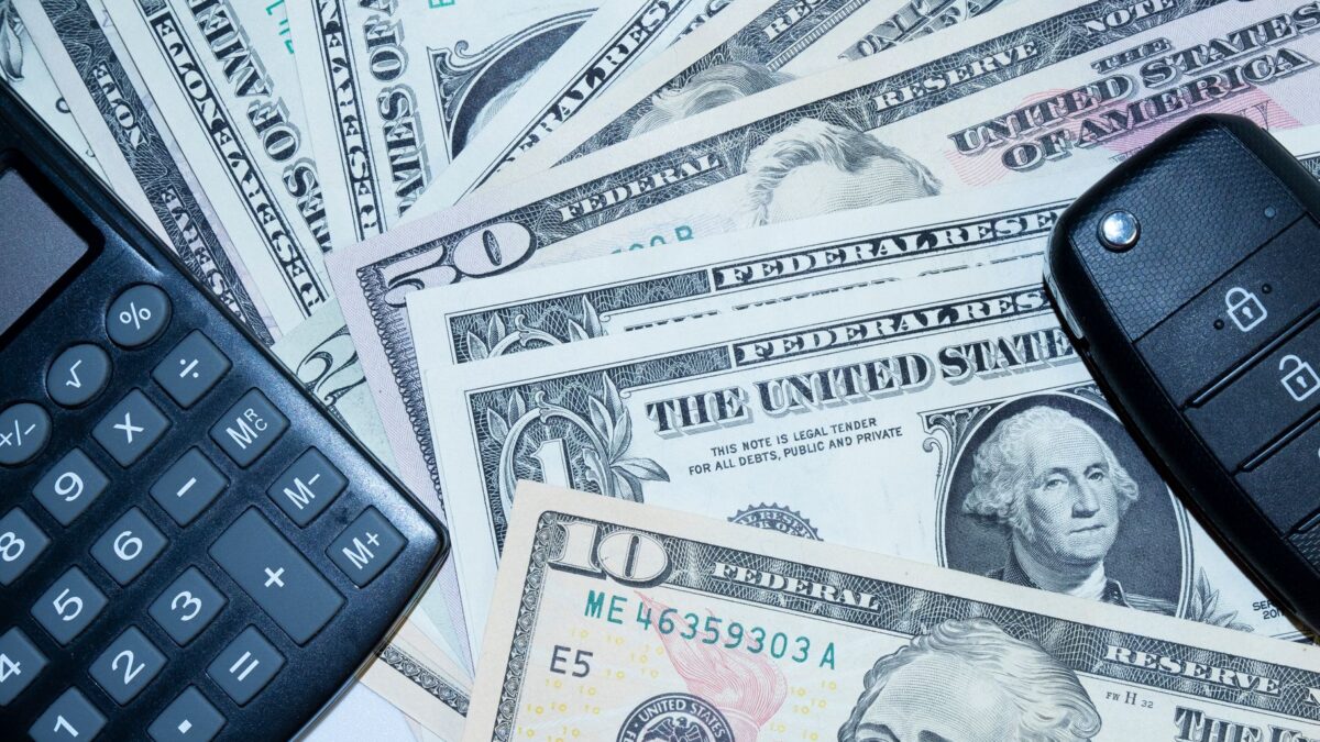 Chaves de carro, calculadora e notas de dólar representando o dinheiro juntado em um consórcio