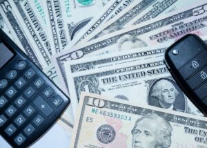 Chaves de carro, calculadora e notas de dólar representando o dinheiro juntado em um consórcio