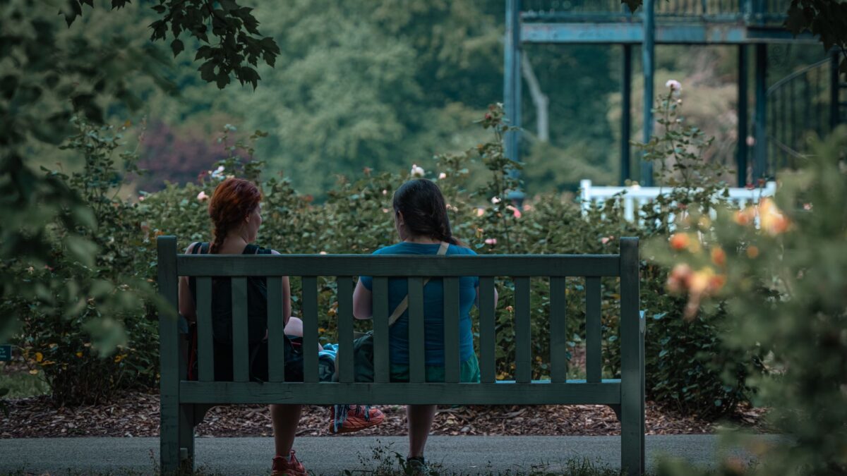 Duas mulheres conversando de verdade em um banco de parque, cercadas de verde