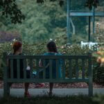 Duas mulheres conversando de verdade em um banco de parque, cercadas de verde