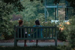 Duas mulheres conversando de verdade em um banco de parque, cercadas de verde