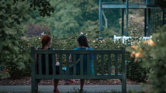 Duas mulheres conversando de verdade em um banco de parque, cercadas de verde