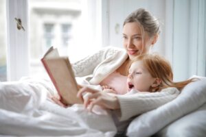 Mãe lendo um livro com a filha, deitadas na cama, em momento de leitura afetiva