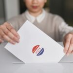Eleitora colocando cédula em urna de votação, ilustrando o 2º turno das Eleições 2026