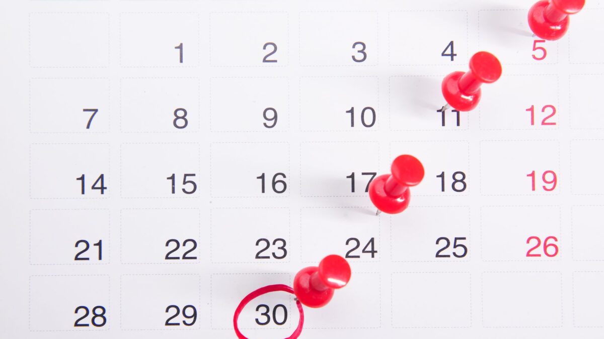 Calendário de mesa com pregadores vermelhos marcando datas importantes, simbolizando prazos