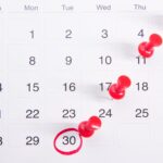 Calendário de mesa com pregadores vermelhos marcando datas importantes, simbolizando prazos
