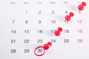 Calendário de mesa com pregadores vermelhos marcando datas importantes, simbolizando prazos