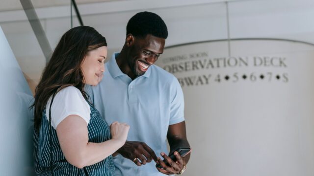 Dois amigos conversando e rindo olhando o celular numa estacao de metro nos EUA