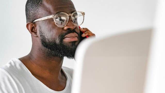 Homem concentrado falando ao telefone, em frente a um laptop, em cena de comunicação do dia a dia