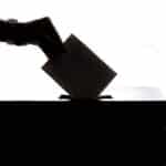 Silhueta de uma mão depositando uma cédula em urna de votação, simbolizando o 2º turno das eleições