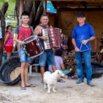 Trio de forró tocando sanfona, zabumba e triângulo ao ar livre no interior do Brasil
