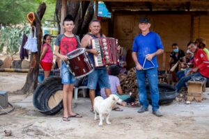 Trio de forró tocando sanfona, zabumba e triângulo ao ar livre no interior do Brasil