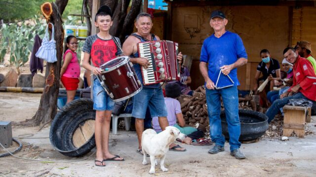 Trio de forró tocando sanfona, zabumba e triângulo ao ar livre no interior do Brasil