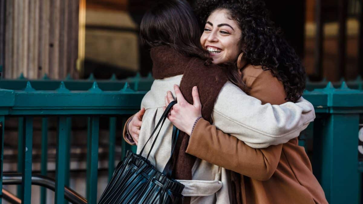 Duas amigas se abraçando e se cumprimentando na rua, ilustrando o contato físico mais próximo da cultura brasileira