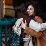 Duas amigas se abraçando e se cumprimentando na rua, ilustrando o contato físico mais próximo da cultura brasileira