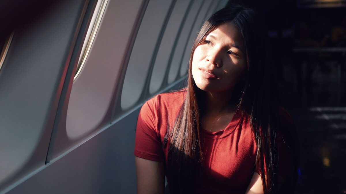 Mulher sentada em avião, olhando pensativa pela janela durante uma viagem