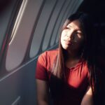 Mulher sentada em avião, olhando pensativa pela janela durante uma viagem