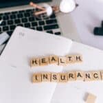 Peças de Scrabble formando as palavras "Health Insurance" sobre um planner, ao lado de um notebook