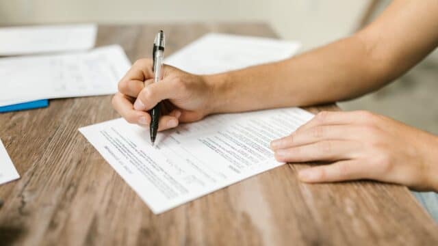 Mão preenchendo formulário em papel com caneta, representando o preenchimento de formulário de imigração