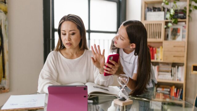 Mãe e filha interagem com um laptop em casa, em cena de vida familiar
