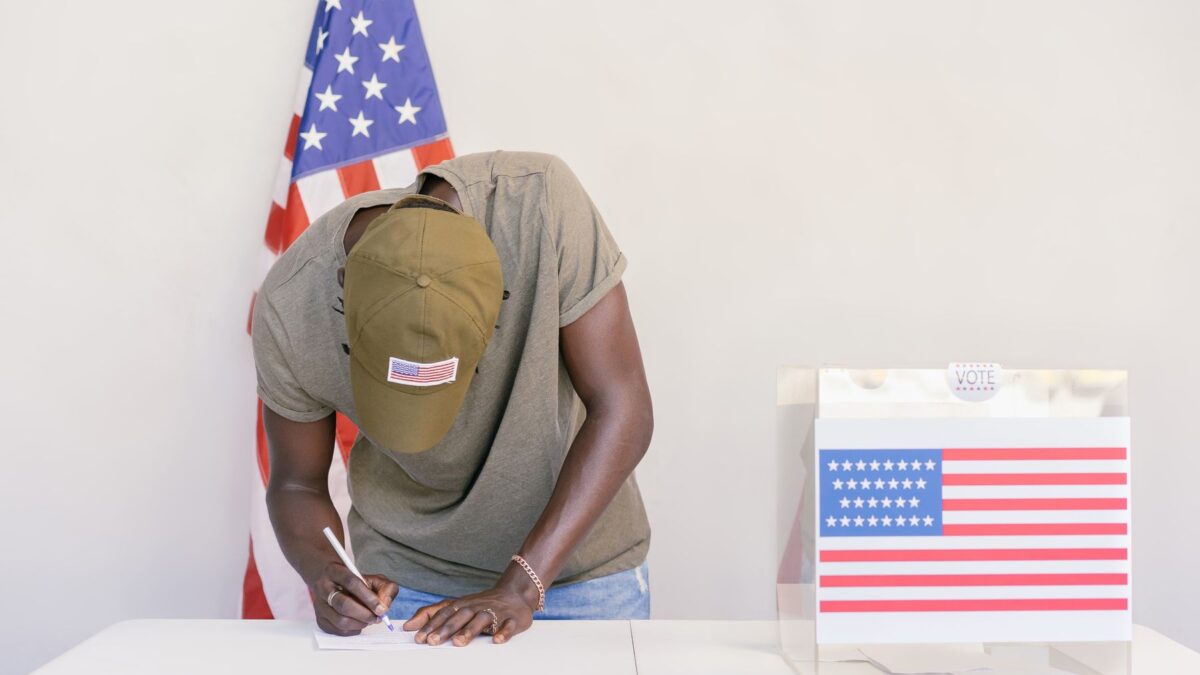 Homem votando em urna com bandeira dos Estados Unidos ao fundo