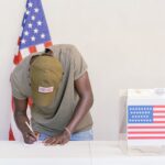 Homem votando em urna com bandeira dos Estados Unidos ao fundo