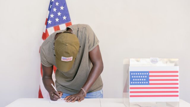 Homem votando em urna com bandeira dos Estados Unidos ao fundo